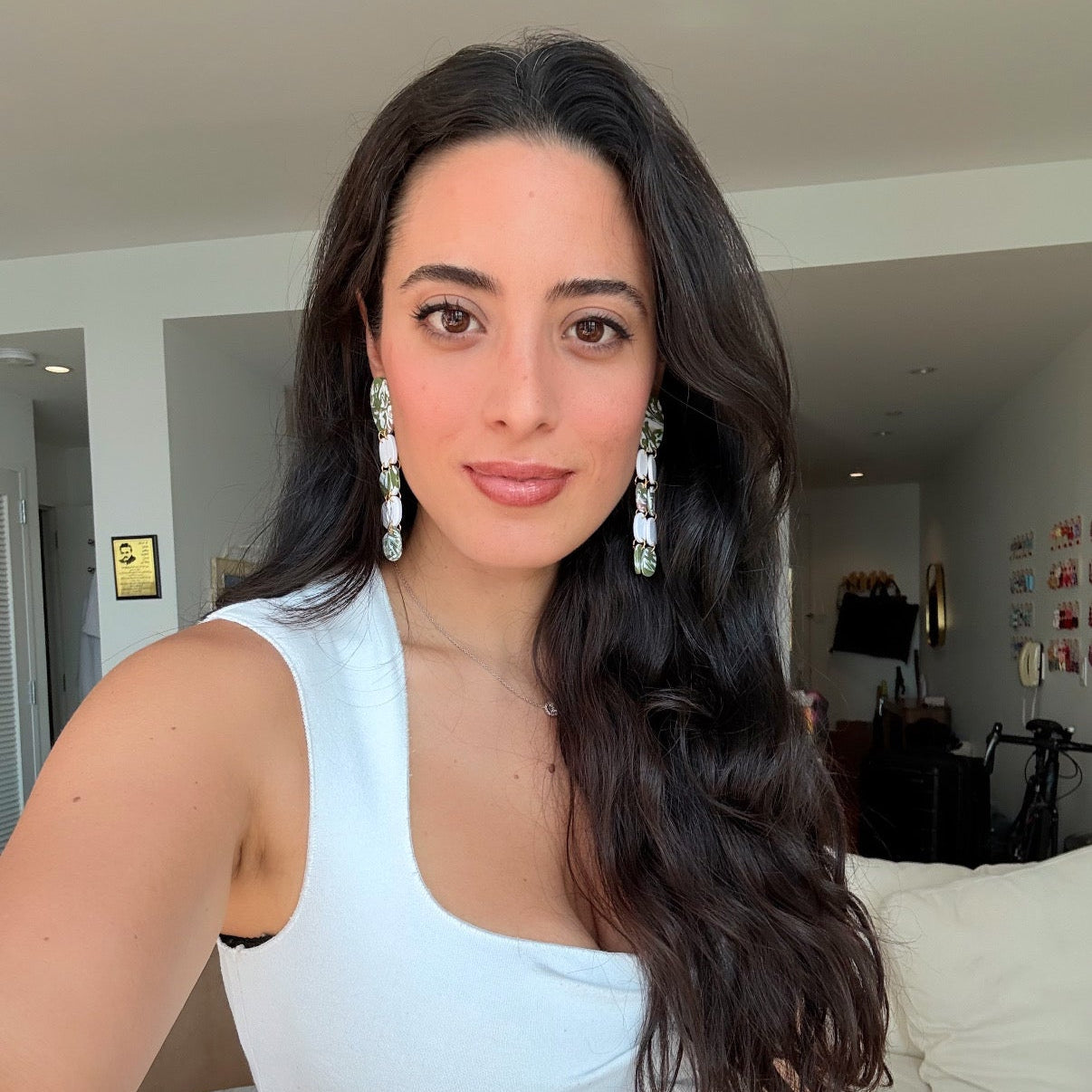 Woman with long dark hair and statement green and white earrings.