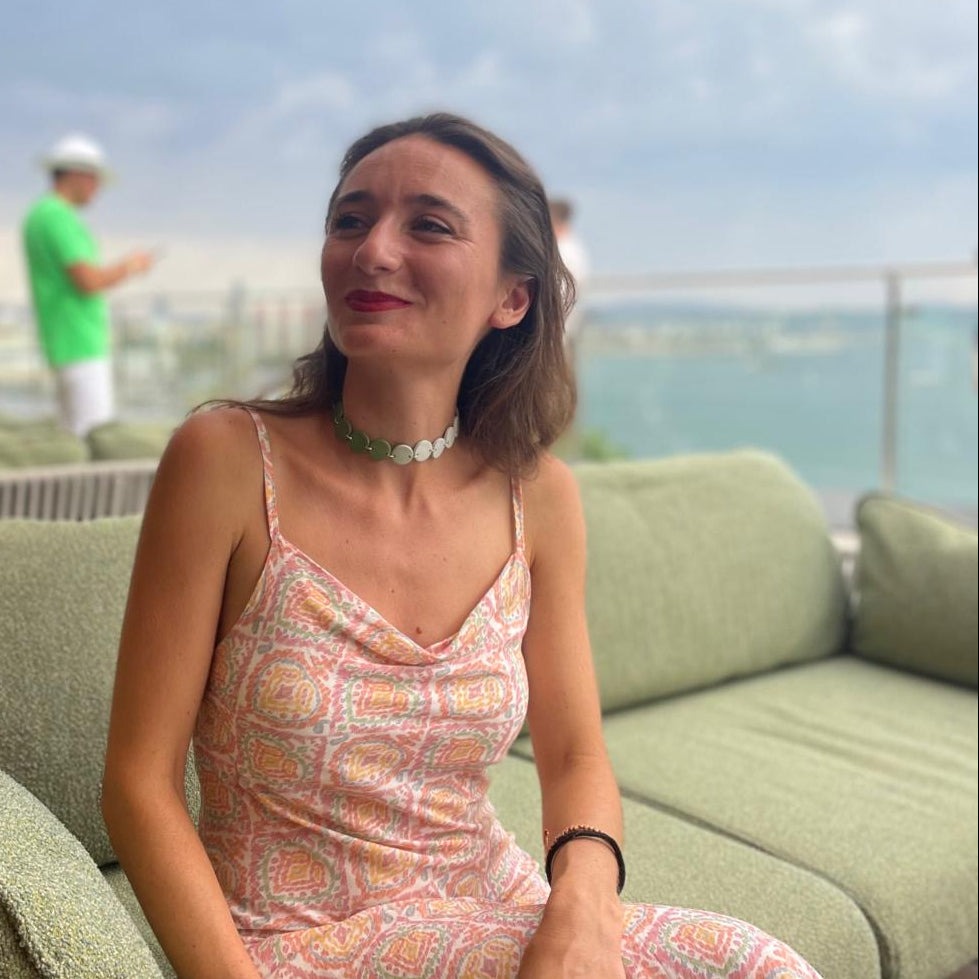 Woman in a patterned dress sitting on a green couch with a scenic background