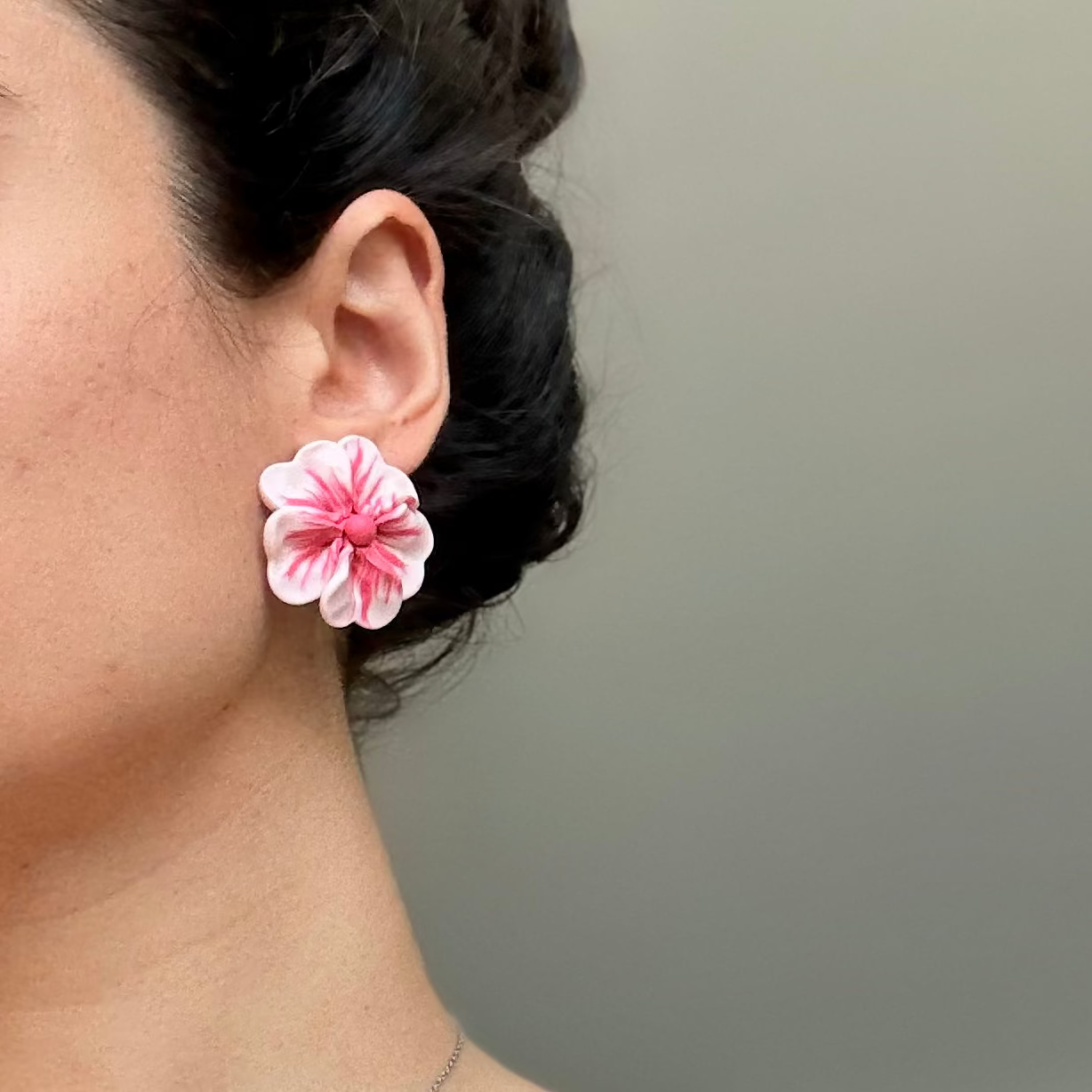 Close-up of a person wearing pink floral earrings with a neutral background