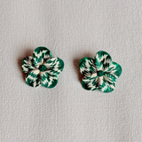 Pair of green and white marbled flower-shaped earrings on a light gray background