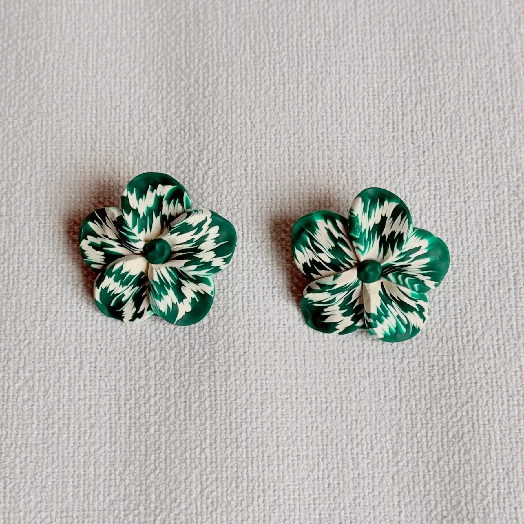 Pair of green and white marbled flower-shaped earrings on a light gray background