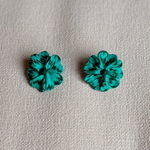 Pair of teal flower-shaped earrings on a beige fabric background