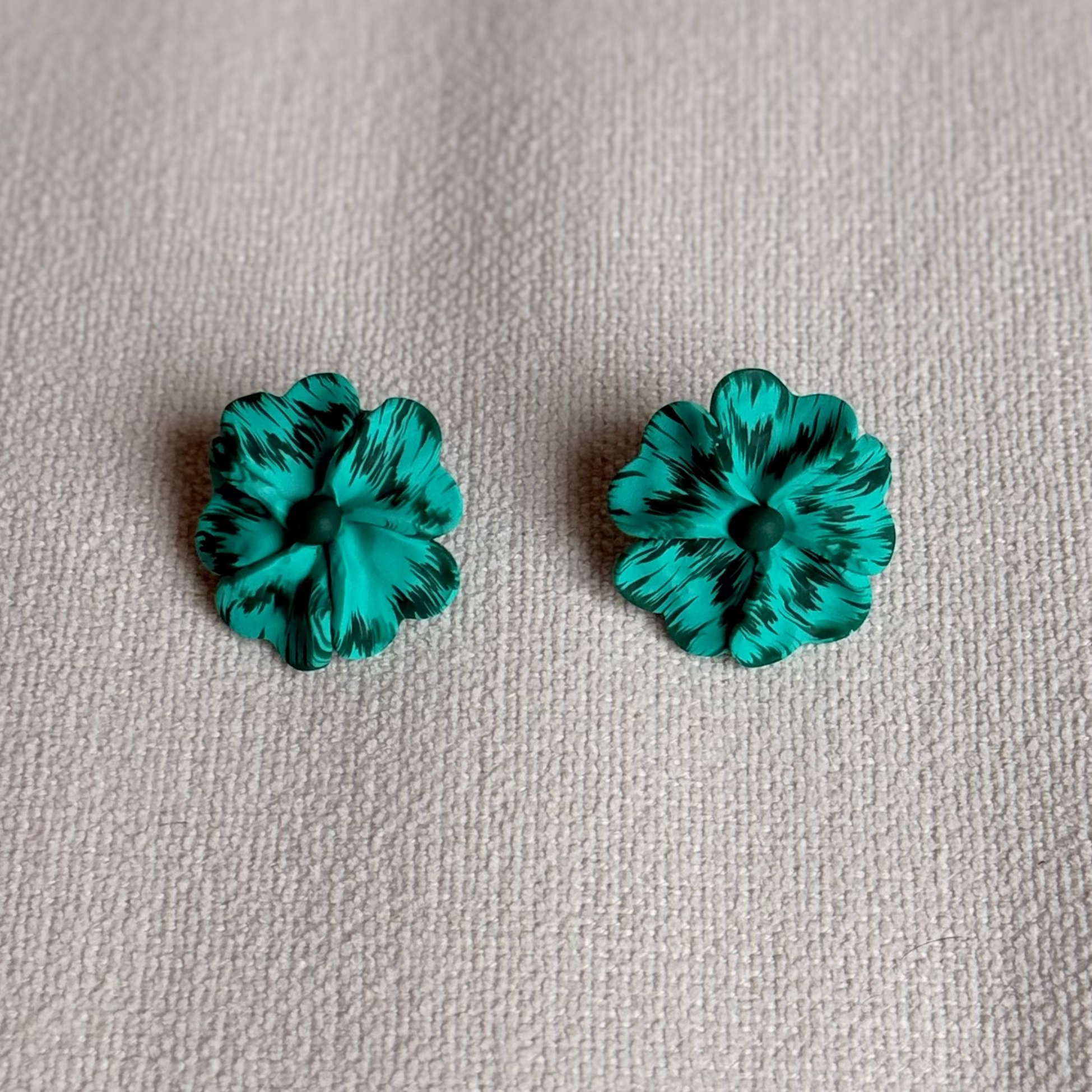 Pair of teal flower-shaped earrings on a beige fabric background