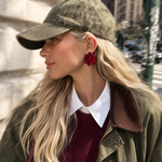 Woman wearing a green cap, green jacket, red sweater, and red earrings on a city street.