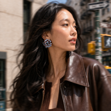 Woman wearing a brown leather jacket and sweater on a city street.